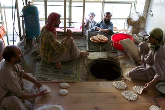 Calling for more bread for a customer, while others flatten the dough, make grooves in it, put it into the tandoor and fetch it baked.